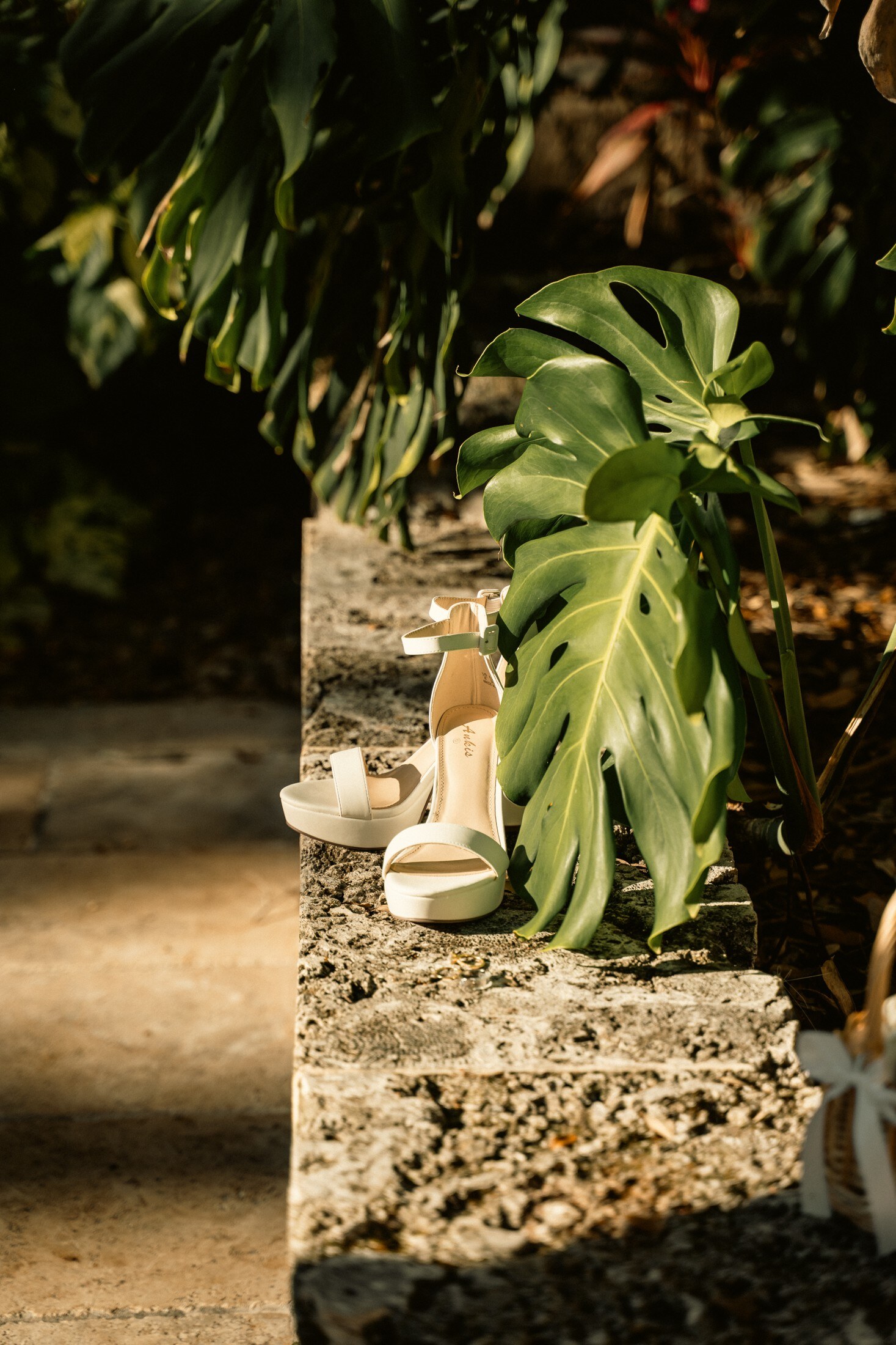 Wedding shoes resting on coral stone beside tropical leaves